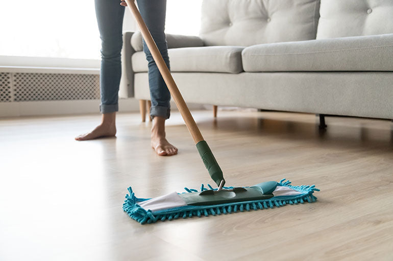 Photo of woman using dust mop on hardwood flooring.